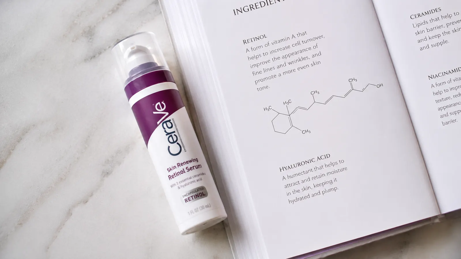 CeraVe Retinol Serum bottle on a marble surface next to an open skincare ingredient reference book, flat lay editorial