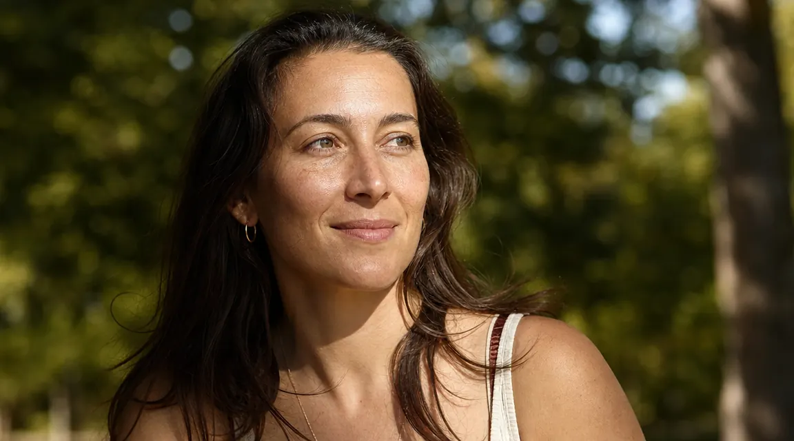 Woman outdoors in morning sunlight, confident relaxed expression, healthy glowing skin